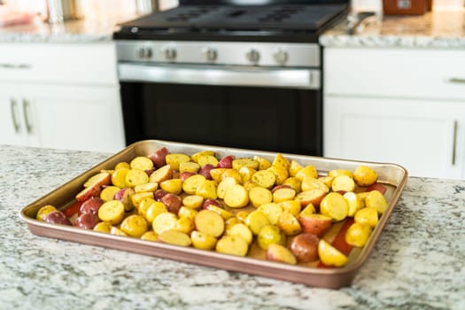 In a modern kitchen, an array of halved, multicolored marble potatoes are arranged on a baking pan lined with a silicone liner. The roasting process infuses the kitchen with a mouthwatering aroma, indicating a delicious side dish in the making.