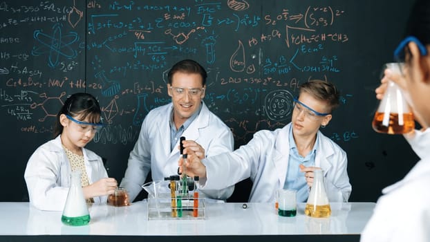 Smart teacher explain about chemical theory while student mixing colored solution or doing experiment. Instructor teaching chemistry while pointing at blackboard in STEM science class. Edification.