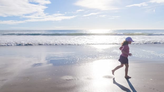 A little girl joyfully plays on the vast, empty sands of El Capitan State Beach in California during winter.