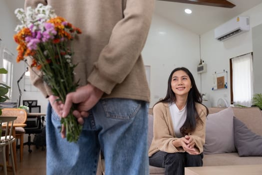 Romantic young asian couple embracing with holding flowers and smiling in living room at home. fall in love. Valentine concept.