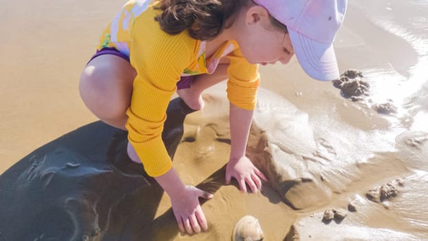 Little girl joyfully clamming on Pismo Beach, bundled up for the winter chill as she explores the sands for seashells and clams.