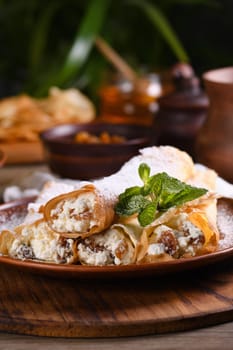 Thin pancakes filled with cottage cheese, honey and raisins, rolled in the form of a tube, sprinkled with powdered sugar, garnished with mint. Festive dish for the pagan Slavic holiday Maslenitsa