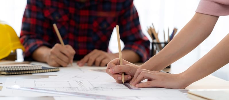 Cropped image of cooperative architect team decide and work together on meeting table with house model, safety helmet and architectural plan scatter around. Closeup. Focus on hand. Burgeoning.