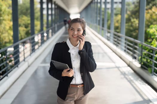 Young Asian business woman wearing suit using smartphone standing on city street outdoors.