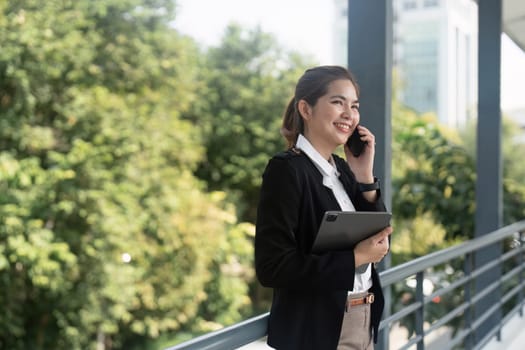 Young Asian business woman wearing suit using smartphone standing on city street outdoors.