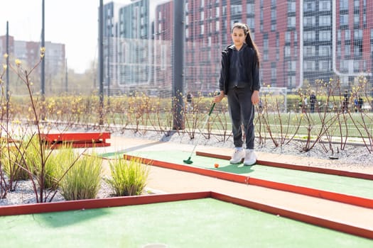 Beautiful toddler european model child girl posing with mini golf equipment on green field outdoor in tropical resort