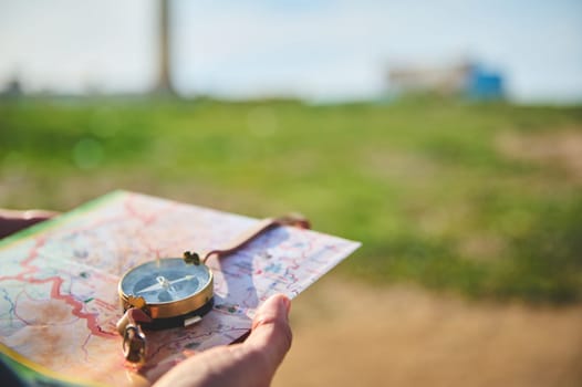 Close-up tourist's hand holds a compass with magnetic arrow showing north direction, over a map against lighthouse background. Copy advertising space. People and travel. Tourism. Adventure. Hiking