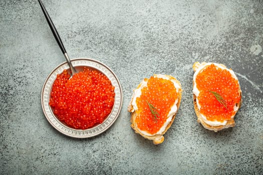 Small metal plate with red salmon caviar and two caviar toasts canapé on grey concrete background, festive luxury delicacy and appetizer.