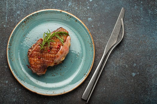 Delicious roasted duck breast fillet with golden crispy skin, with pepper and rosemary, top view on ceramic blue plate, rustic concrete rustic background.