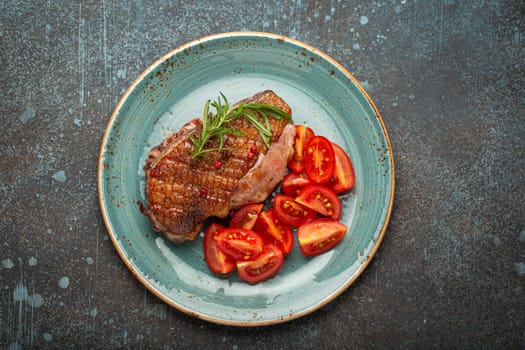 Delicious roasted duck breast fillet with golden crispy skin, with pepper and rosemary, top view on ceramic blue plate served with cherry tomatoes salad, rustic concrete rustic background