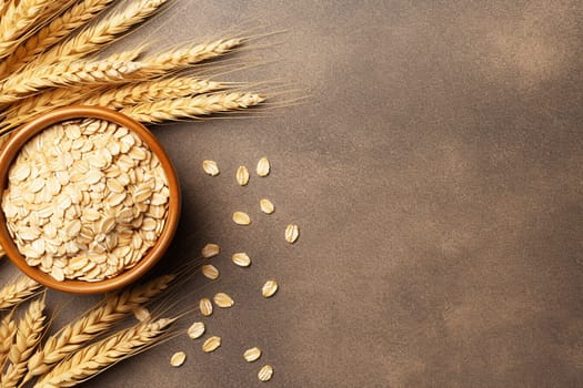 Golden wheat ears and grains in bowl on brown surface.