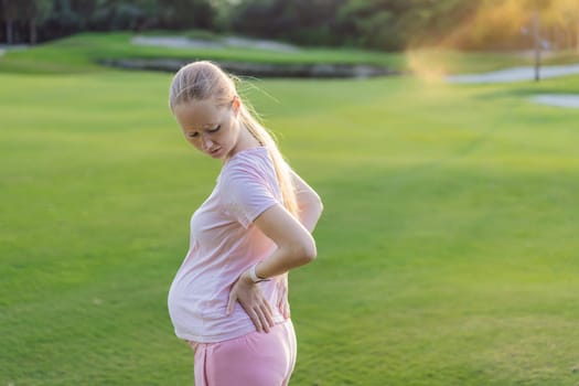 Expectant woman experiences back pain outdoors, seeking relief and comfort during pregnancy with a gentle outdoor stretch or rest.