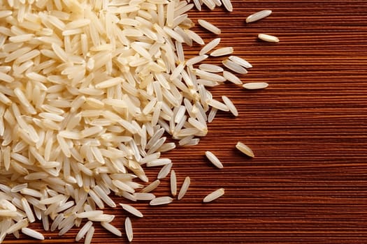 Uncooked white rice grains spread across a wooden surface.