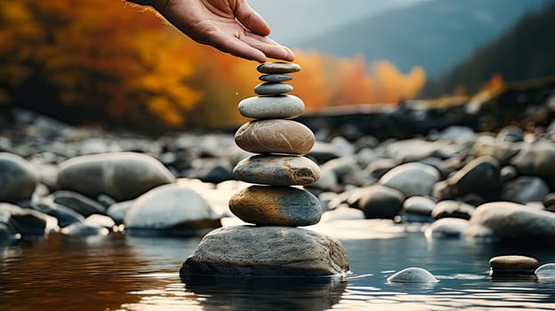 Witness the meditative artistry as a mans hand skillfully places stones one atop the other, creating a captivating balance. A tranquil and harmonious moment.