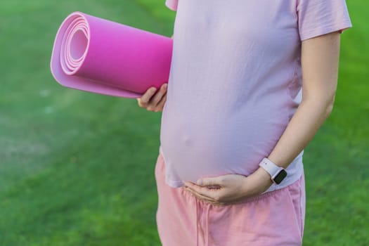 Energetic pregnant woman takes her workout outdoors, using an exercise mat for a refreshing and health-conscious outdoor exercise session.