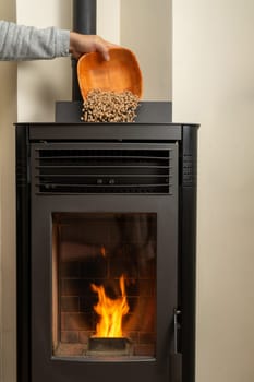 Man's hand loading a pellet stove with a minbre bowl, it needs to be refilled regularly for the device to function properly