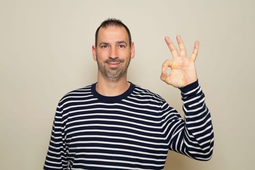 Portrait of a cheerful hispanic man showing ok gesture isolated on beige background