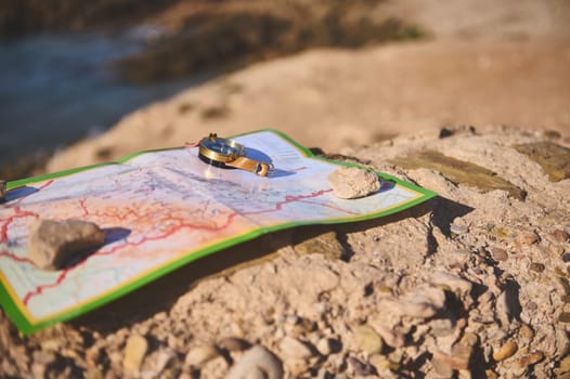 A geographic map and nautical equipment, a compass on the rock against the background of a cliff overlooking the Atlantic rock beach. Trip. Tour tourism. Adventure and travel concept