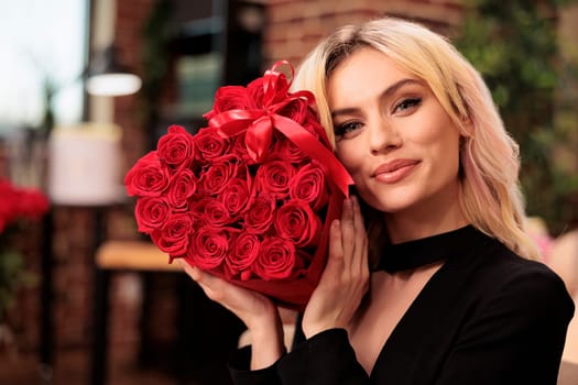 Lovely girlfriend posing with valentines day red roses bouquet, receiving romantic gift from boyfriend during love holdiday. Cute woman smiling at camera, holding flowers in heart shaped box