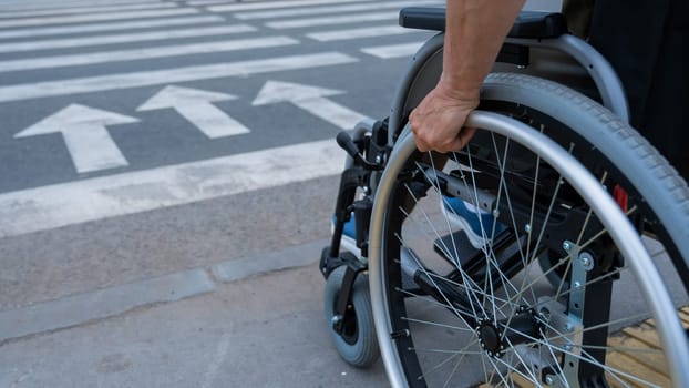 Rear view of an elderly woman in a wheelchair going to a pedestrian crossing. Close-up on wheels