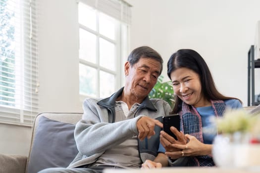 Portrait of Asian adorable senior couple using smartphone together video chatting with family in living room at home..