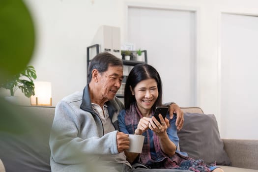 Portrait of Asian adorable senior couple using smartphone together video chatting with family in living room at home..