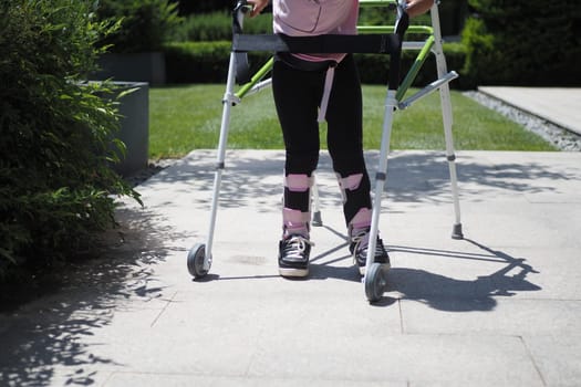 child with walking frame and knee orthosis outdoor .