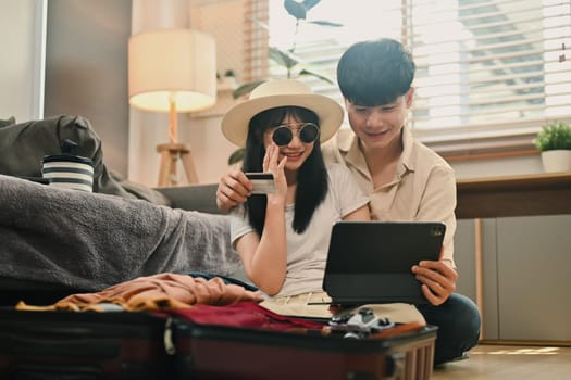Young couple sitting near suitcases and booking tickets or hotel on web. Holiday summer vacation concept.