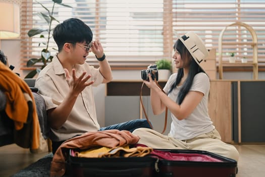 Happy Asian couple preparing for honeymoon vacation, packing clothes into suitcase.