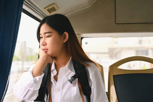 Young woman looking through looking through the window while commuting by bus.