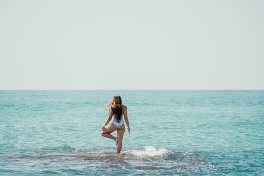 Woman sea yoga. Back view of free calm happy satisfied woman with long hair standing on top rock with yoga position against of sky by the sea. Healthy lifestyle outdoors in nature, fitness concept.