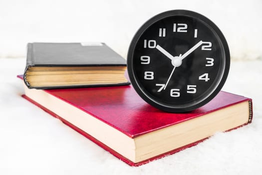 Close up Black alarm clock and book stacked on table