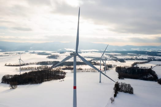 Fly over wind turbines and windmills in the winter field at sunlight. Clean and renewable energy sources concept.