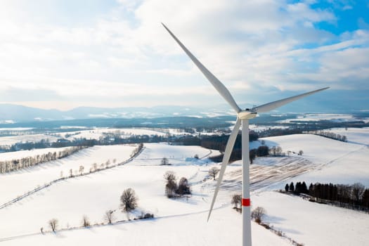 Wind mills or wind turbines in the field in winter with mountains on the background.