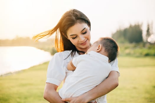 In a quiet park at dusk, a mother holds her sleeping baby, feeling warmth of setting sun. Her face is full of love and contentment as she takes in the beauty of garden. A perfect Mother's Day moment