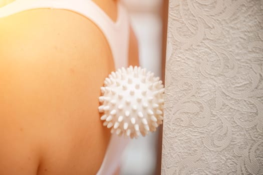 Athletic slim caucasian woman doing thigh self-massage with a massage ball indoors. Self-isolating massage.