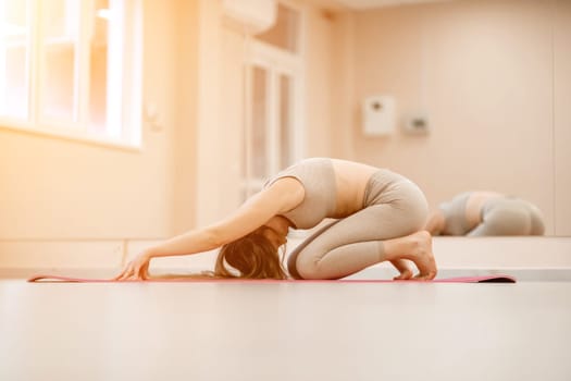 Girl does yoga. Young woman practices asanas on a beige one ton background