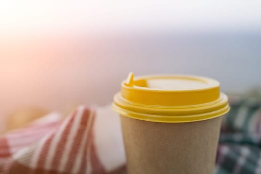 Yellow cup with lid, coffee against a backdrop of a blue sky and sea. Illustrating cup and beverage.