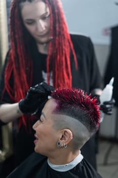 The hairdresser removes excess dye from the skin of a female with a cotton pad.Asian woman with a short haircut in a hairdressing salon