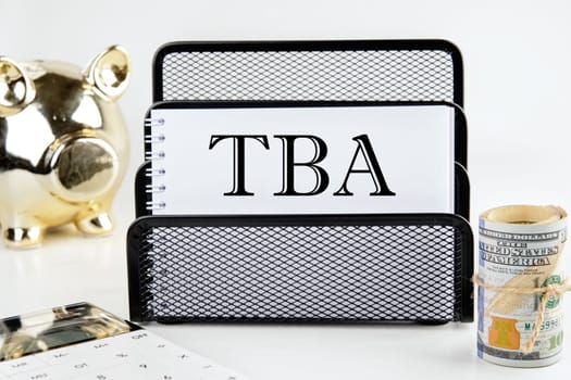 TBA text on a white piece of paper next to a piggy bank, a roll of money and a calculator on a white background