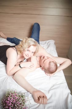 Loving enamored adult couple communicates, embraces, and has fun alone together on the bed in the bedroom or hotel room. The woman is wearing tank top and the man is shirtless