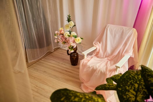 Delicate pink bright interior of the room with an armchair, vase with roses, draped curtains and a window. Location and background in the photo studio