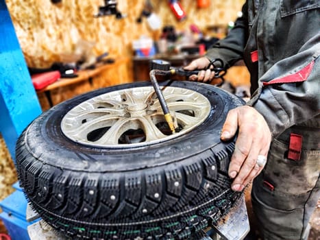 Ishim, Russia - November 27, 2023: Mechanic repairs a car wheel and makes a tire in a dirty garage. Replacement of summer wheels, tires for winter indoors
