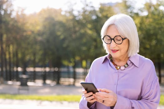 senior woman using mobile phone outdoors, concept of technology and elderly people leisure, copy space for text