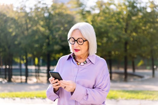 senior woman using mobile phone outdoors, concept of technology and elderly people leisure