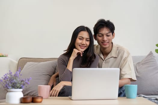 Young couple asian using laptop together while sitting on sofa at home.