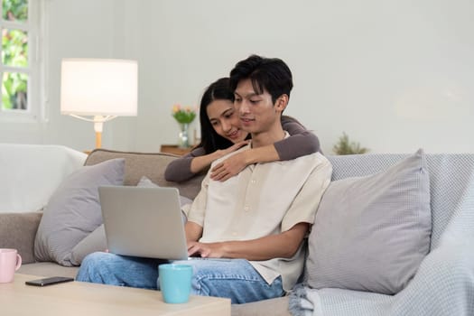 Young couple asian using laptop together while sitting on sofa at home.