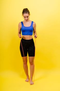 Fit female athlete with jumping with rope during fitness training against yellow background