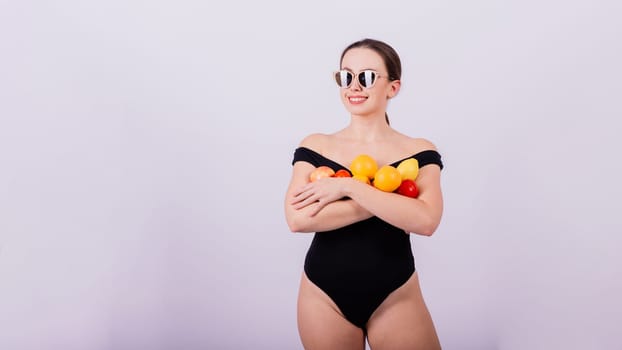 A female holding an apples, lemons, oranges in different arms isolated on grey background.