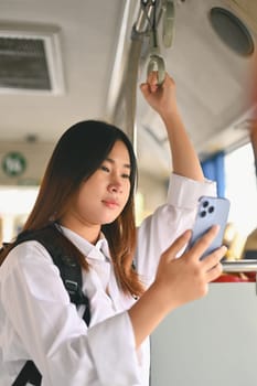 Portrait of young woman with backpack using mobile phone in public transport.